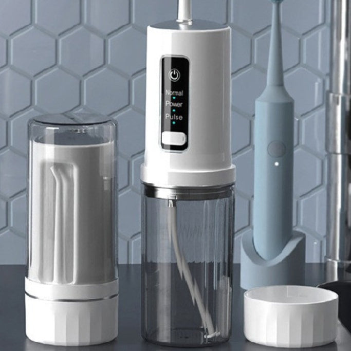 White dental water flosser with clear container on a gray surface against a tiled wall background